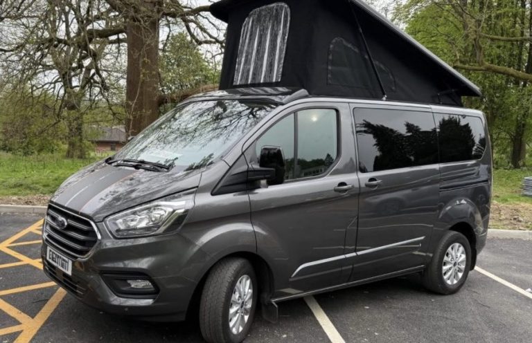 A grey camper van with a raised roof parked in a wooded area.
