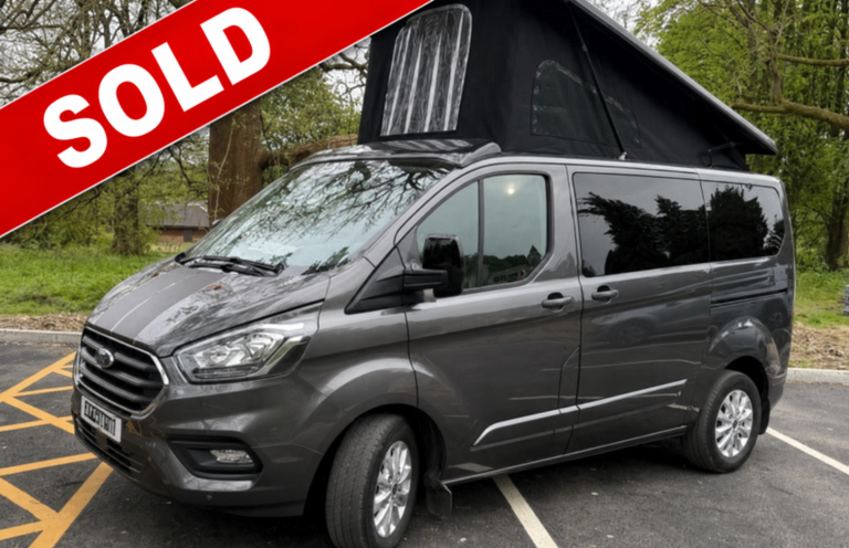 A grey camper van with a raised roof parked in a wooded area.